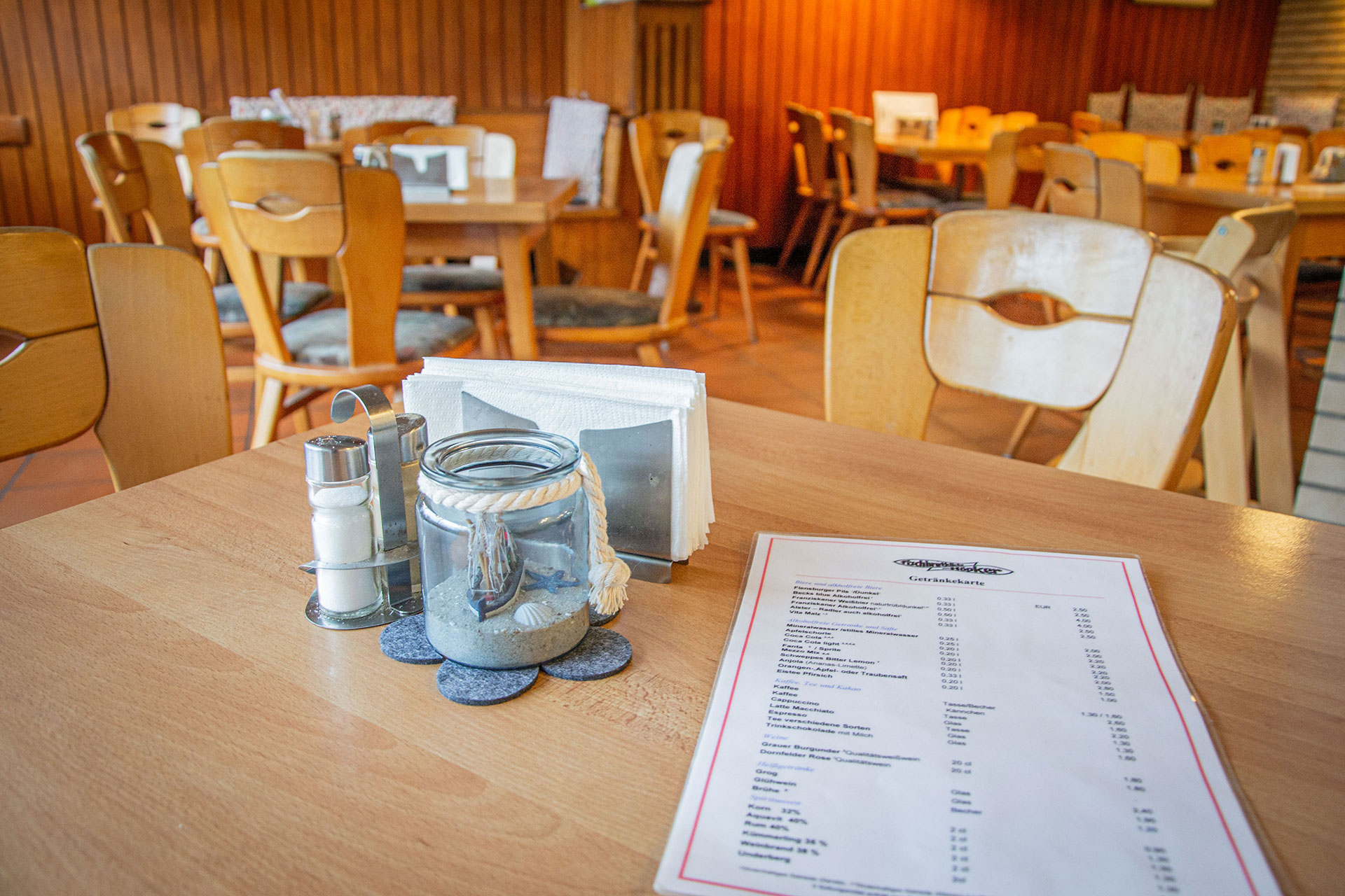 Eine Getränkekarte liegt auf einem Tisch, daneben stehen ein Salzstreuer, Pfefferstreuer und eine Kerze.