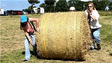 Die Teilnehmer des ostfrisieschen Mehrkampfes rollen einen Rundballen über die Wiese. 