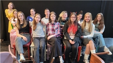 Gruppenfoto von Jugendlichen des Theaterlabors 3 des Stadttheaters Bremerhaven, sitzend und stehend in Kostümen und Alltagskleidung vor schwarzem Bühnenhintergrund.