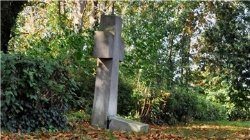 Kreuz aus Stein an einer Hecke.