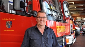 Ein Mann mit Brille steht vor mehreren Feuerwehrautos.