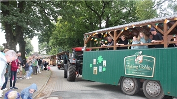 Traktoren ziehen Festwagen über eine Dorfstraße. Am Rand stehen Menschen. 