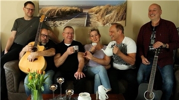 Fünf Männer und eine Frau mit Instrumenten und Kaffeetassen sitzen auf einem Sofa, Band 3t 4 Coffee