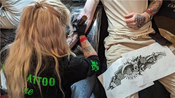 Eine Tätowiererin aus den Niederlanden sticht ein Tattoo auf einen Arm eines Besuchers.