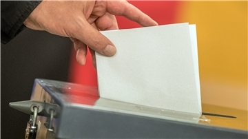 Ein Wahlzettel wird in die Wahlurne gesteckt. 