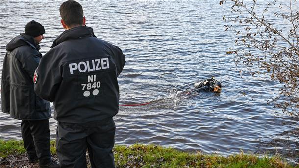 Carsten Hodis, Polizeitaucher aus Oldenburg, sucht im Stoteler See nach einer Schusswaffe.  Zwei Männer schauen vom Ufer aus zu.