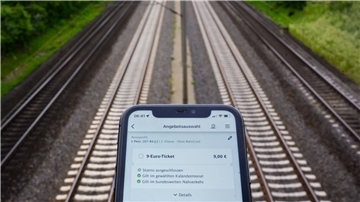 Vor Bahnschienen ist auf einem Smartphonedisplay die Bahn-App DB Navigator zu sehen