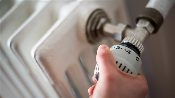 Eine Frau dreht am Thermostat einer Heizung. 