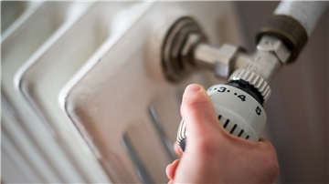Eine Frau dreht am Thermostat einer Heizung. 