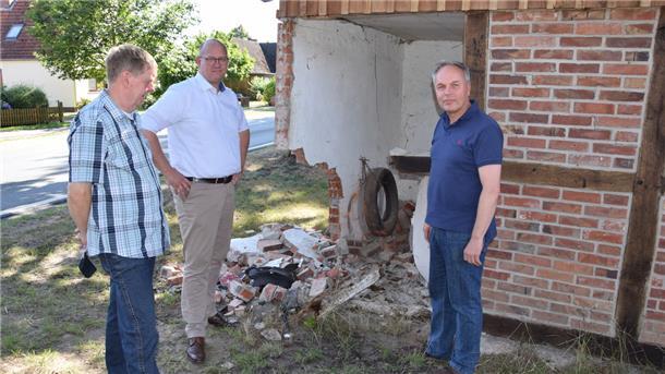 Abermals ist die Garage an der Selsinger Straße in Ostrhade beschädigt: Bürgermeister Marco Mohrmann (Mitte), sein Stellvertreter Thomas Brunckhorst (links) und Rüdiger Meyer vom „Hof Stoffers“ an der Unfallstelle.