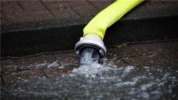 Abgepumptes Wasser aus einem Haus fließt aus einem Schlauch auf die Straße.