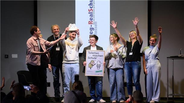 Abgesandte der Hellweg Realschule in Unna-Massen (Nordrhein-Westfalen) stehen zusammen mit Moderator „Checker“ Julian Janssen (l) bei der Verleihung der Hauptpreise des bundesweiten Wettbewerbs „Toiletten machen Schule“ beim 1. Deutschen Schultoilettengipfel der German Toilet Organization (GTO) auf der Bühne.