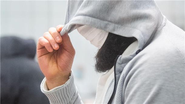 Abu Walaa, mutmaßlicher Anführer der Terrormiliz Islamischer Staat (IS) in Deutschland, steht im Oberlandesgericht hinter einer Glasscheibe.