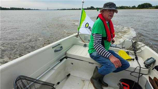 Ein Mann mit Hut sitzt in einem offenen Boot, das auf der Weser fährt.
