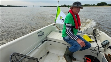 Ein Mann mit Hut sitzt in einem offenen Boot, das auf der Weser fährt.
