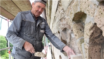 Ein Maurer setzt bei einer Kirchenmauer einen Stein ein.