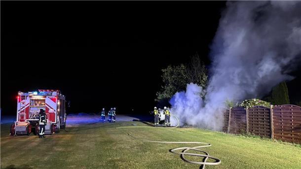 Einsatzkräfte der Feuerwehr löschen einen brennenden Holzstapel.