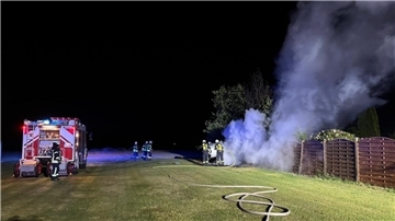 Einsatzkräfte der Feuerwehr löschen einen brennenden Holzstapel.