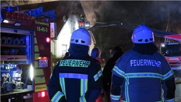 Feuerwehrleute gucken auf ein brennendes Haus