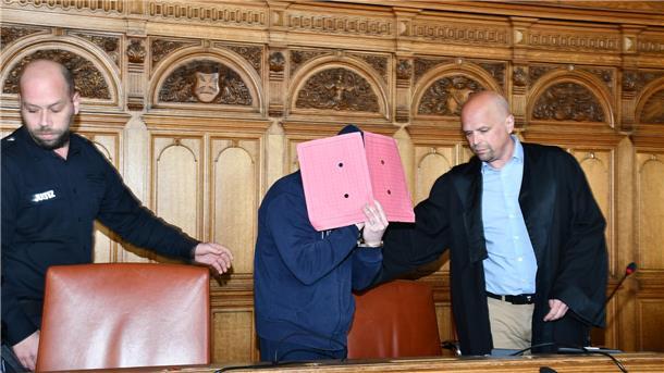 Angeklagter wird mit Mappe vorm Gesicht zum Platz geführt