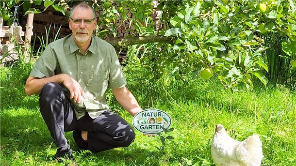 Peter Allhusen hält in seinem Garten das Zertifikat "Naturgarten" in der Hand