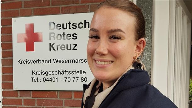 Eine junge Frau vor dem Schild des DRK Wesermarsch. Altenpflegerin Chariece Hübler ist im DRK-Kreisverband für die Pflegeberatung zuständig.