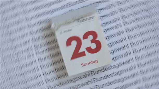 Das Foto zeigt einen Abreißkalender, der den 23. Februar 2025 anzeigt. Dahinter ist ein weißes Blatt Papier mit der mehrfachen Aufschrift Bundestagswahl zu sehen.