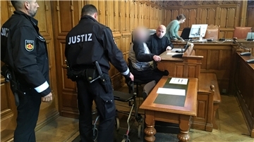 Justizbeamte vor der Anklagebank mit dem Angeklagten und dessen Anwalt.