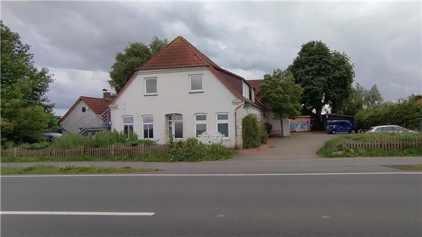 Das Foto zeigt ein altes Haus samt Nebengebäuden an einer Straße.