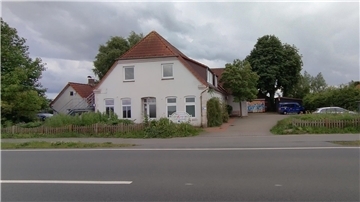 Das Foto zeigt ein altes Haus samt Nebengebäuden an einer Straße.