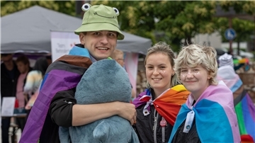 Bild von drei jungen Menschen, die lustige Kostüme und bunte Regenbogenfahnen tragen.