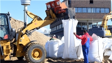 Arbeiter befüllen mit einem Radlader Sandsäcke. 