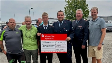 Gruppenfoto mit sechs Männern, darunter Vertreter der Feuerwehr in Uniform, die einen symbolischen Scheck über 4.500 Euro für die Jugendfeuerwehr Beverstedt präsentieren.
