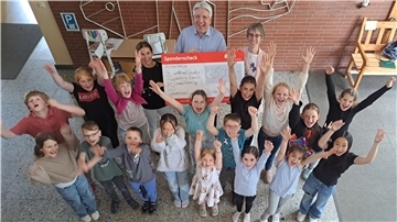 Das Foto zeigt viele Grundschüler und drei Erwachsene mit einem großen Scheck. Es ist bei einer Scheckübergabe in der Grundschule St. Willehad in Nordenham entstanden.