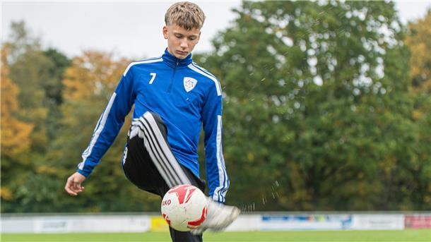 Ein junger Fußballer hält einen Ball hoch.
