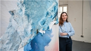 Eine Frau neben einem Bild. Das Bild zeigt eine Wolke und einen Gletscher. Die neue Bremerhaven-Stipendiatin Angelika J. Trojnarski verbindet Kunst und Wissenschaft.