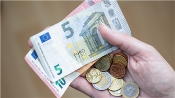 Eine Frau hält Geldscheine und Münzen in der Hand. 