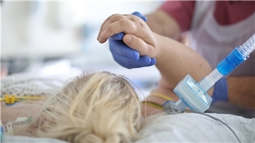 Pflegekraft mit blauen Handschuhen hält die Hand einer beatmeten Patientin auf der Intensivstation.