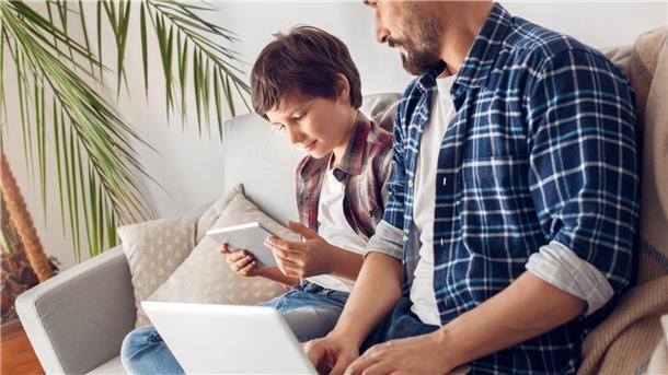 Gesunder Körper, gesunder Geist – wie Eltern ihren Kindern dabei helfen können Vater und Sohn auf der Couch mit Laptop und Ipad