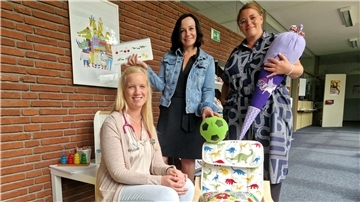 Drei Frauen sitzen und stehen an einem kleinen Tisch mit Spielzeug und einem Kinderstuhl mit Dinosaurier-Muster