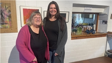 Zwei Damen stehen vor einer Wand mit Bildern. Anke Coldewey (links) führte rund 25 Jahre das Café in der Seefelder Mühle. Nun wird Wiebke Stromitzky ihre Rolle übernehmen.