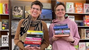 Zwei Frauen stehen vor einem Bücherregal und halten selbst mehrere Bücher in den Händen.