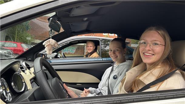Drei Jugendliche sitzen in Autos und schauen durchs geöffnete Fenster in die Kamera.