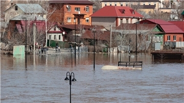 Anwohner stehen an einer Absperrung und beobachten ein überschwemmtes Gebiet im russischen Orenburg.
