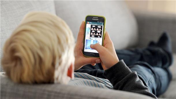 Datenschutzbeauftragter informiert an Schulen ARCHIV - Ein Kind liegt auf einem Sofa und blickt auf sein Smartphone.