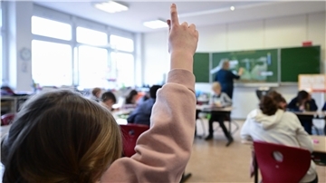 Ein Mädchen hebt im Unterricht in einer Schule den Finger.