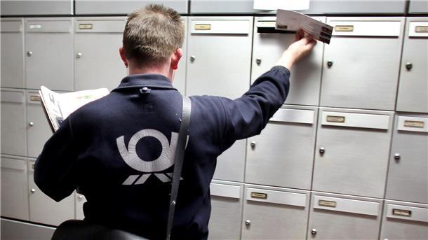 Ein Postzusteller steckt eine Sendung in einen Briefkasten. 