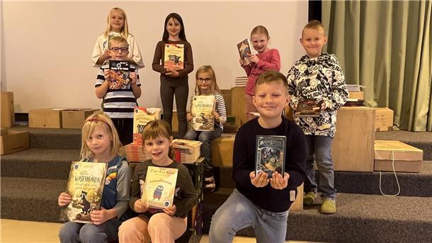 Neun Kinder halten ein Buch und freuen sich. 