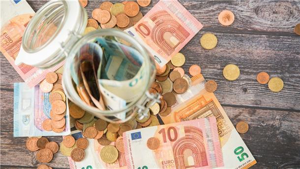 Ein Glas mit Geld sowie umherliegende Geldscheine und -münzen.
