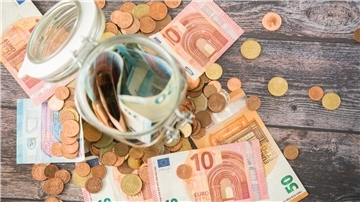 Ein Glas mit Geld sowie umherliegende Geldscheine und -münzen.